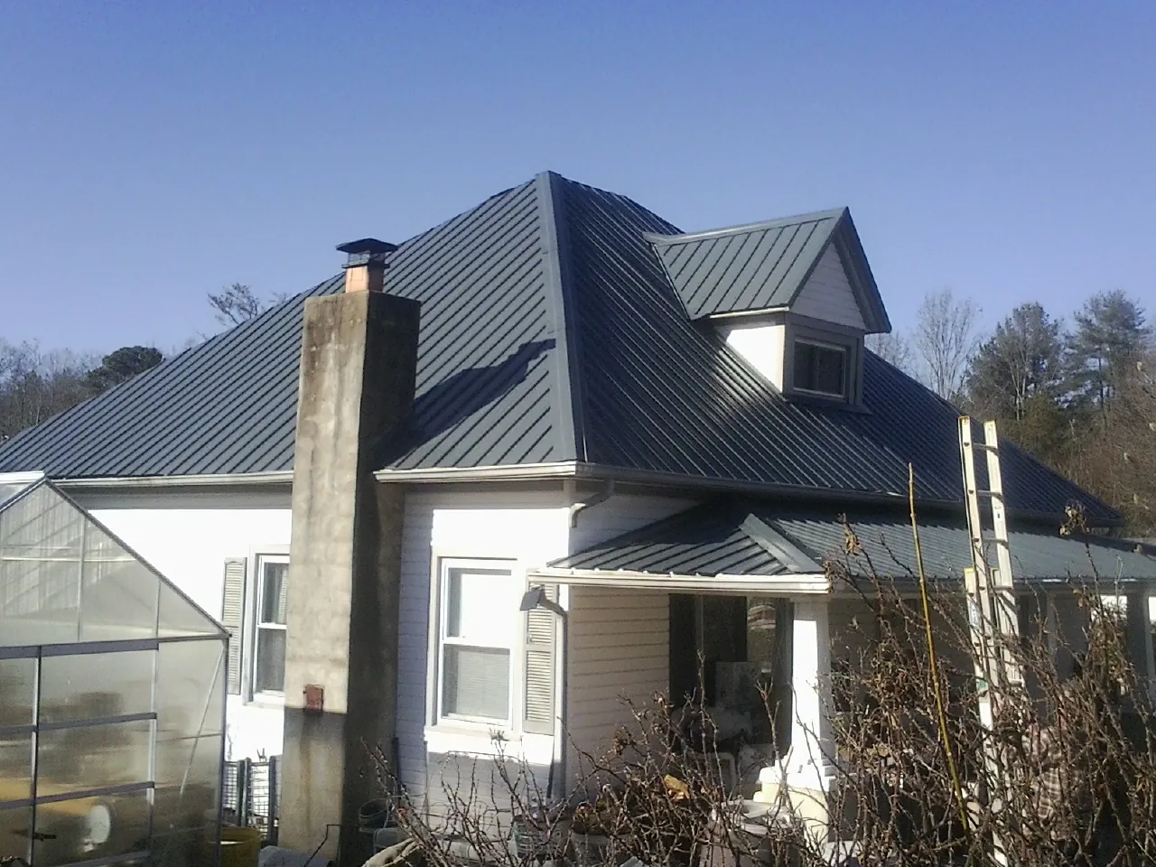 Dark blue standing seam metal roof on a white farmhouse with dormer — Slate & Tile Roof Repair by Roofing Brothers in Waukee