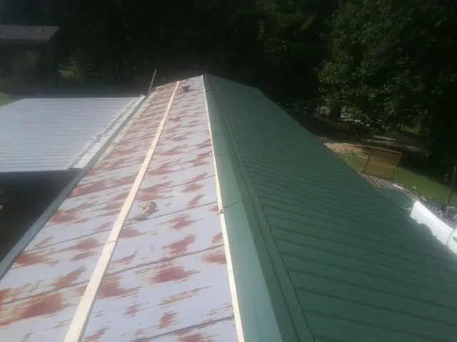 Old rusted panels beside newly installed green metal roofing — Wind Damage Roof Repair by Roofing Brothers in Waukee