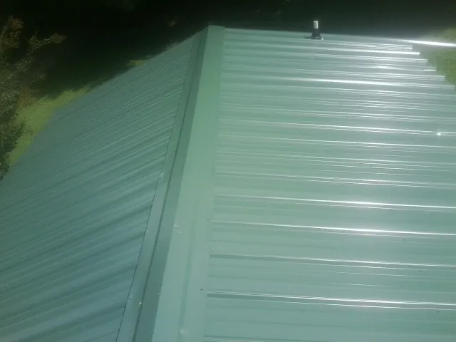 New green metal panels meeting at the ridge of a roof — Flat Roof Repair work by our crew in Waukee