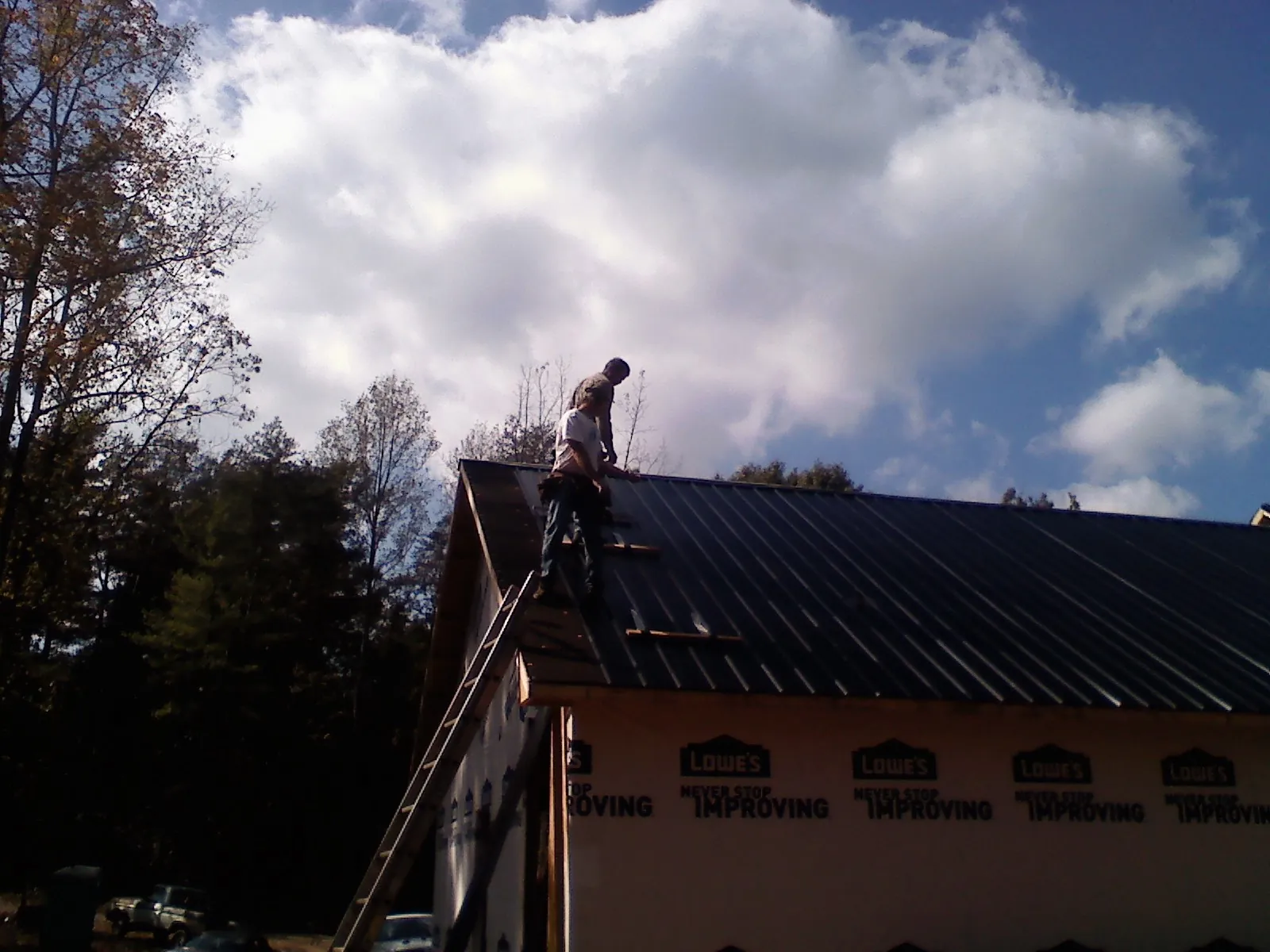 Roofer fastening dark metal panels high against a cloudy sky, from a Roof Inspection job in Waukee