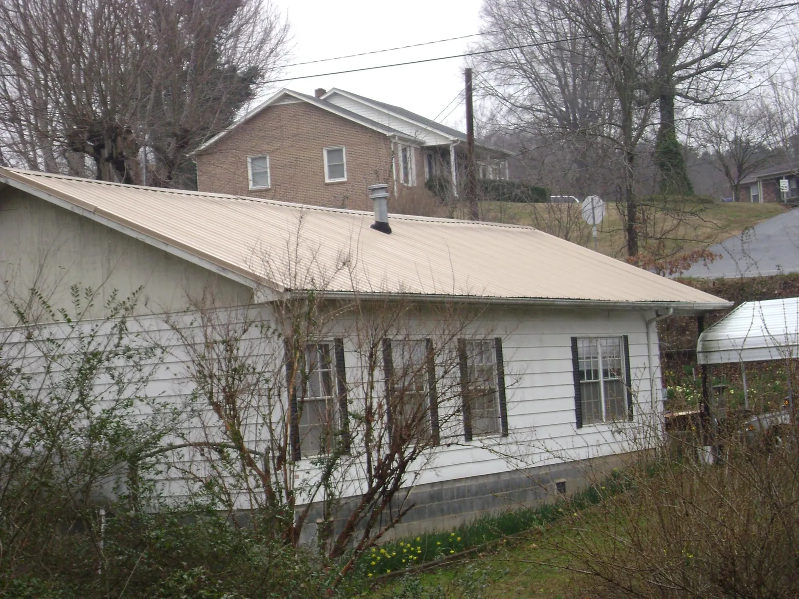 Tan metal roof on a white sided house set into a hillside — Commercial Roofing by Roofing Brothers in Waukee