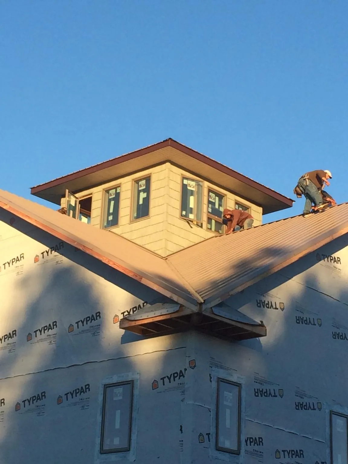 Roofers working around a rooftop cupola on a new metal roof at sunset — Roof Waterproofing in Waukee by Roofing Brothers